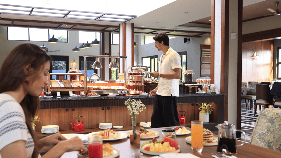  A woman seated at a dining table in a well-lit restaurant area, with a buffet counter visible in the background at The Golden Tusk, Jim Corbett