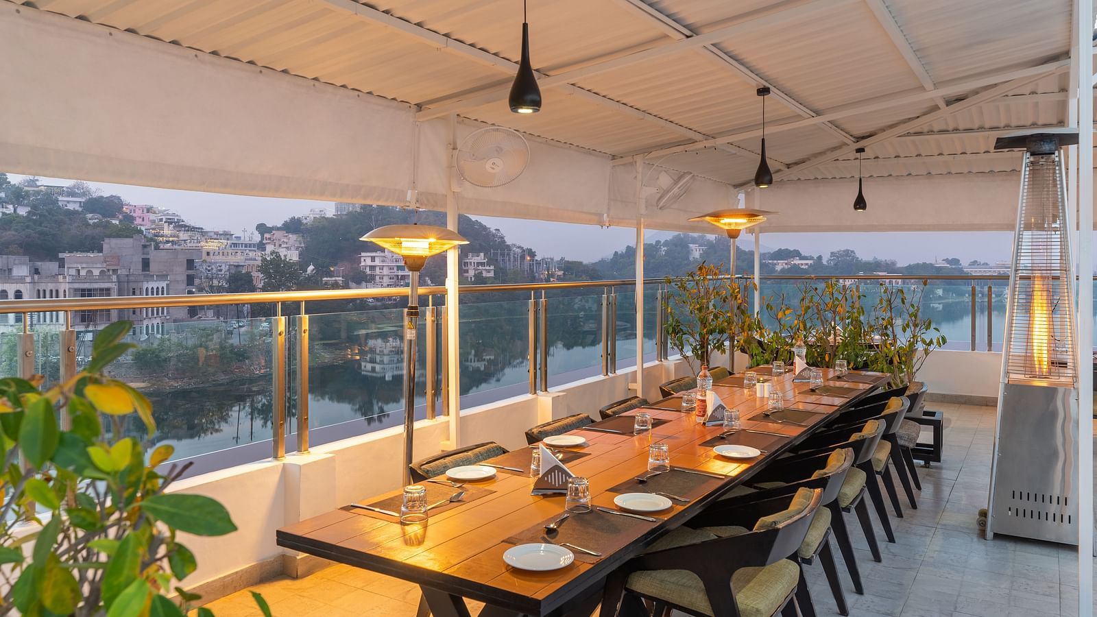 A shot of a large dining table at the rooftop restaurant with plants and ceiling lights - Hotel Rajdarshan, Udaipur.