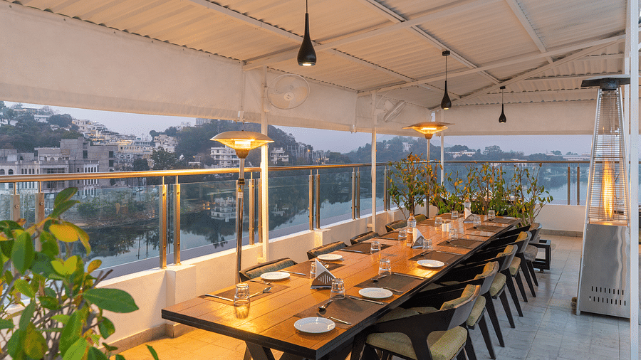 A shot of a large dining table at the rooftop restaurant in udaipur with plants and ceiling lights - Hotel Rajdarshan, Udaipur.