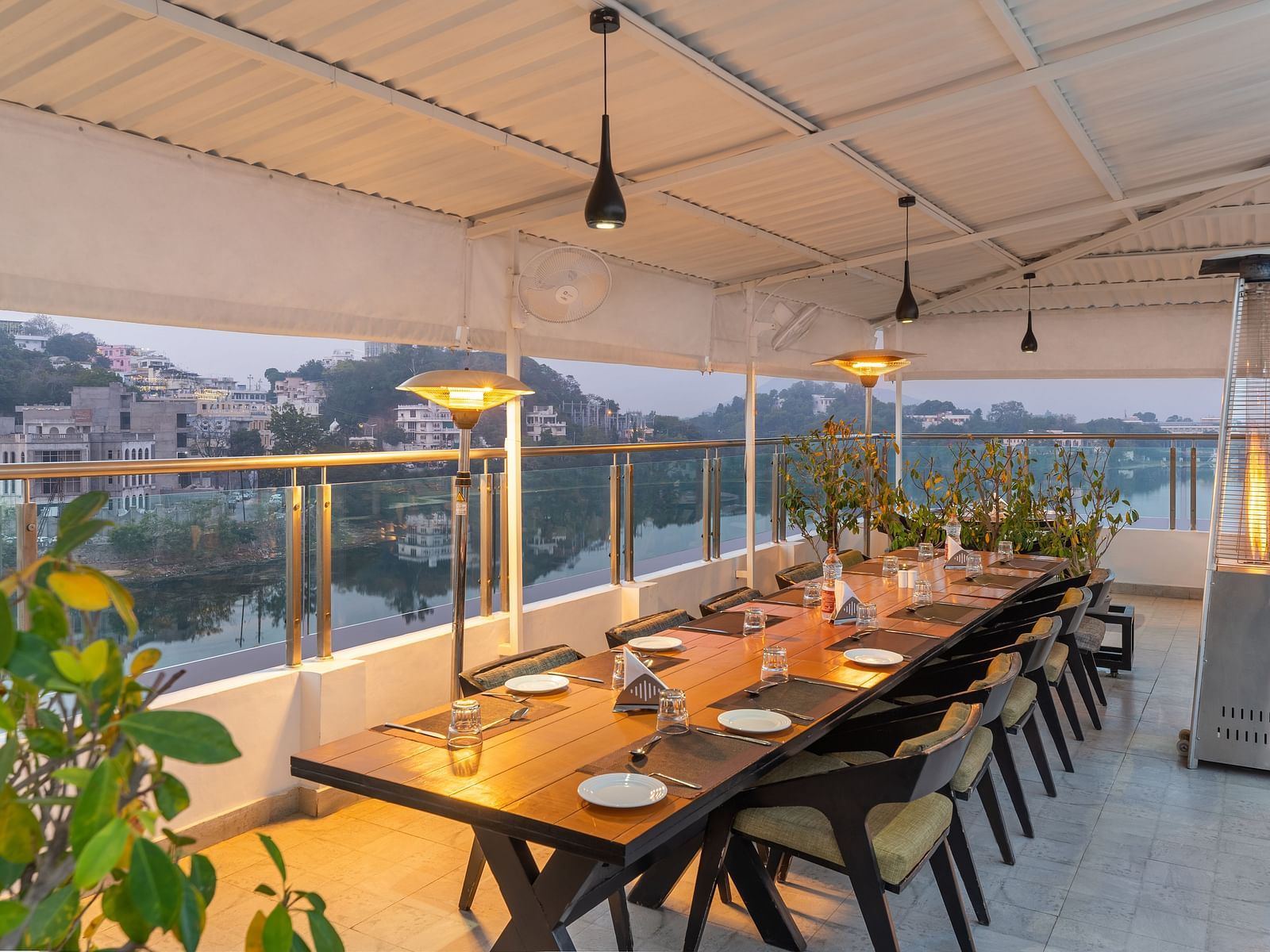 A shot of a large dining table at the rooftop restaurant with plants and ceiling lights - Hotel Rajdarshan, Udaipur.