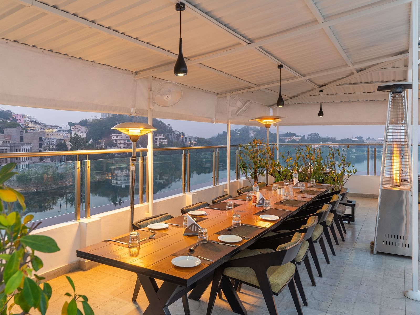 A shot of a large dining table at the rooftop restaurant with plants and ceiling lights - Hotel Rajdarshan, Udaipur.