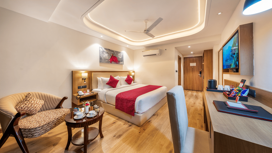 A hotel bedroom at Lords Inn Katra featuring a king size bed, an armchair with a coffee table, a television, and a work desk with a chair.