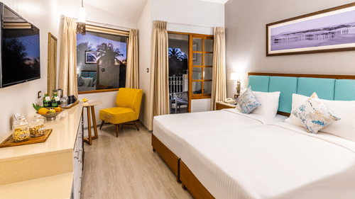 Superior room with double bed, chair, table, tv and a framed art at Heritage Village Resorts & Spa, Goa.