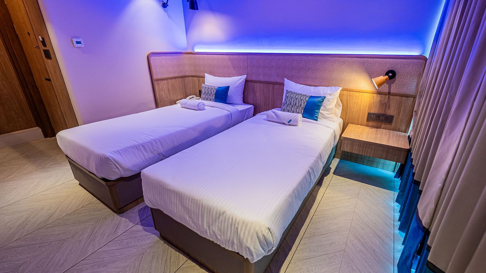 A room at Indie Stays Mumbai International Airport, featuring two single beds with wooden headboards and ambient lighting.
