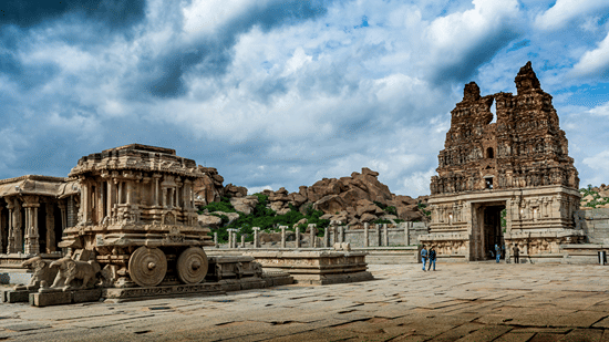 Ancient stone ruins including a chariot temple and gopuram under a cloudy sky