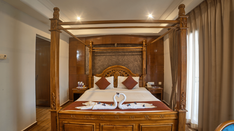 Classic wooden four-poster bed with decorative swan towel art in a warmly lit room at Ilara Hotels & Spa, OMR, Chennai