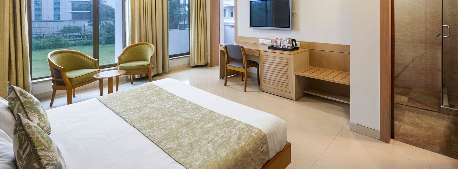 A spacious hotel room at Monday Hotels Mahape, Navi Mumbai, showing the bed, a desk, and the bathroom entrance.