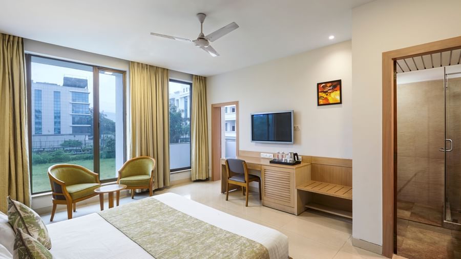 A spacious hotel room at Monday Hotels Mahape, Navi Mumbai, showing the bed, a desk, and the bathroom entrance.