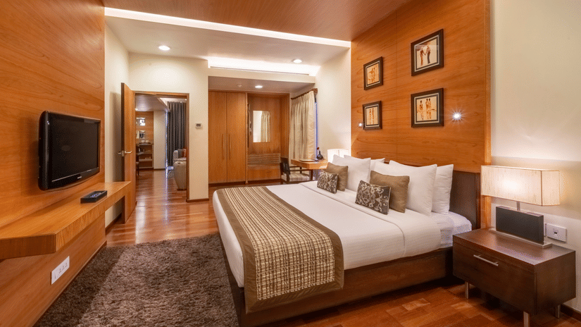 An end-to-end view of the bedroom of Russel Suite with a king size bed, side tables, lamps, a tv and a carpet at Kenilworth Hotel, Kolkata.