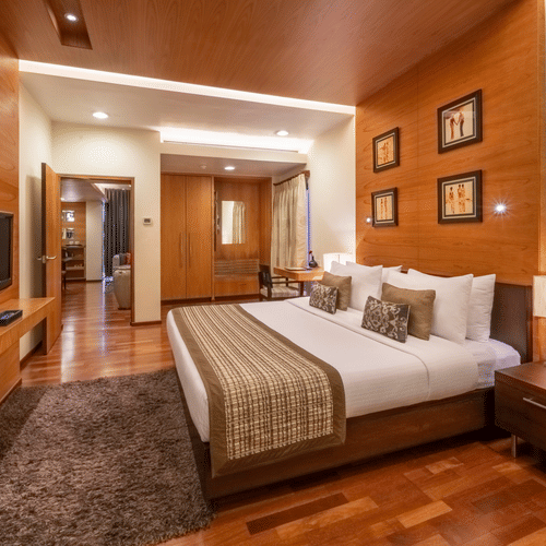 An end-to-end view of the bedroom of Russel Suite with a king size bed, side tables, lamps, a tv and a carpet at Kenilworth Hotel, Kolkata.