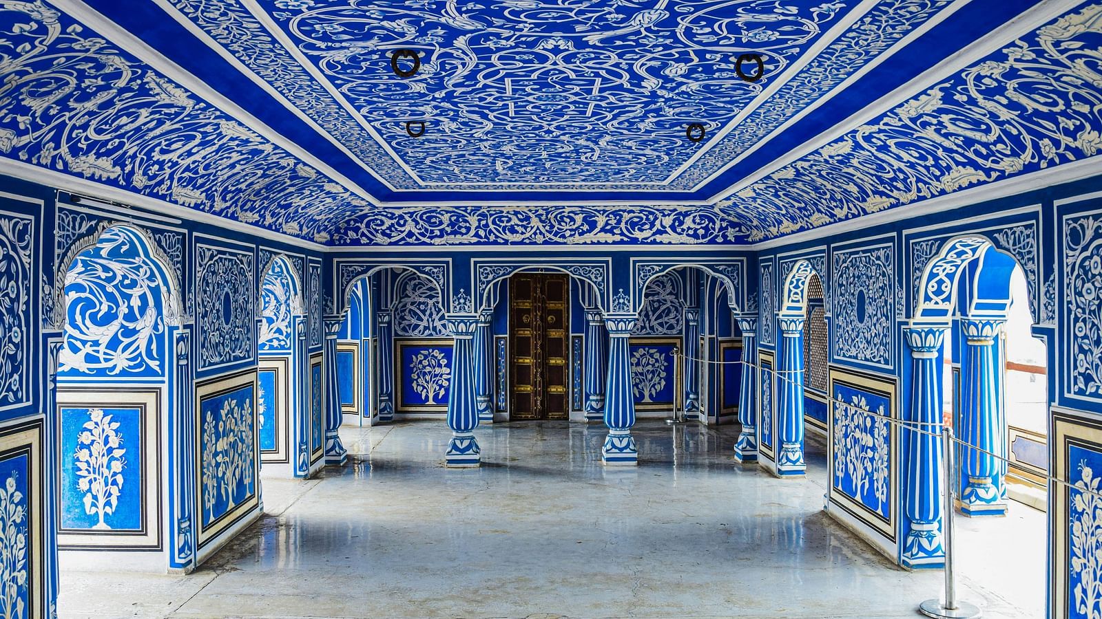 An elaborately decorated hall with blue and white patterns on the walls and ceiling, featuring arched doorways and a polished floor.