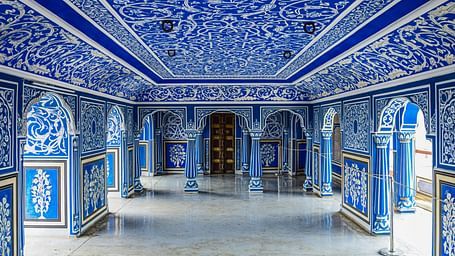 An elaborately decorated hall with blue and white patterns on the walls and ceiling, featuring arched doorways and a polished floor.