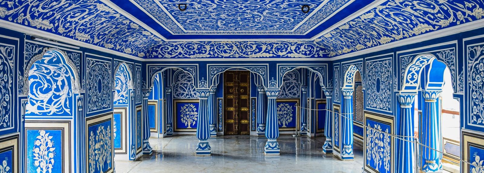 An ornately decorated blue hall with intricate artwork on the walls and ceiling, showcasing traditional Rajasthani architecture and design.