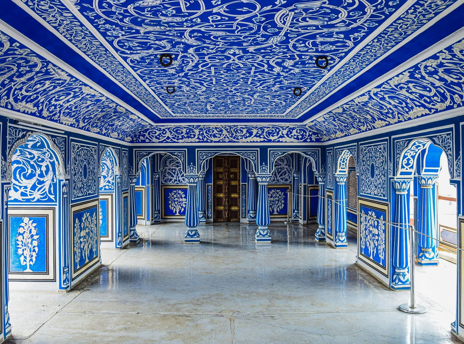 An elaborately decorated hall with blue and white patterns on the walls and ceiling, featuring arched doorways and a polished floor.