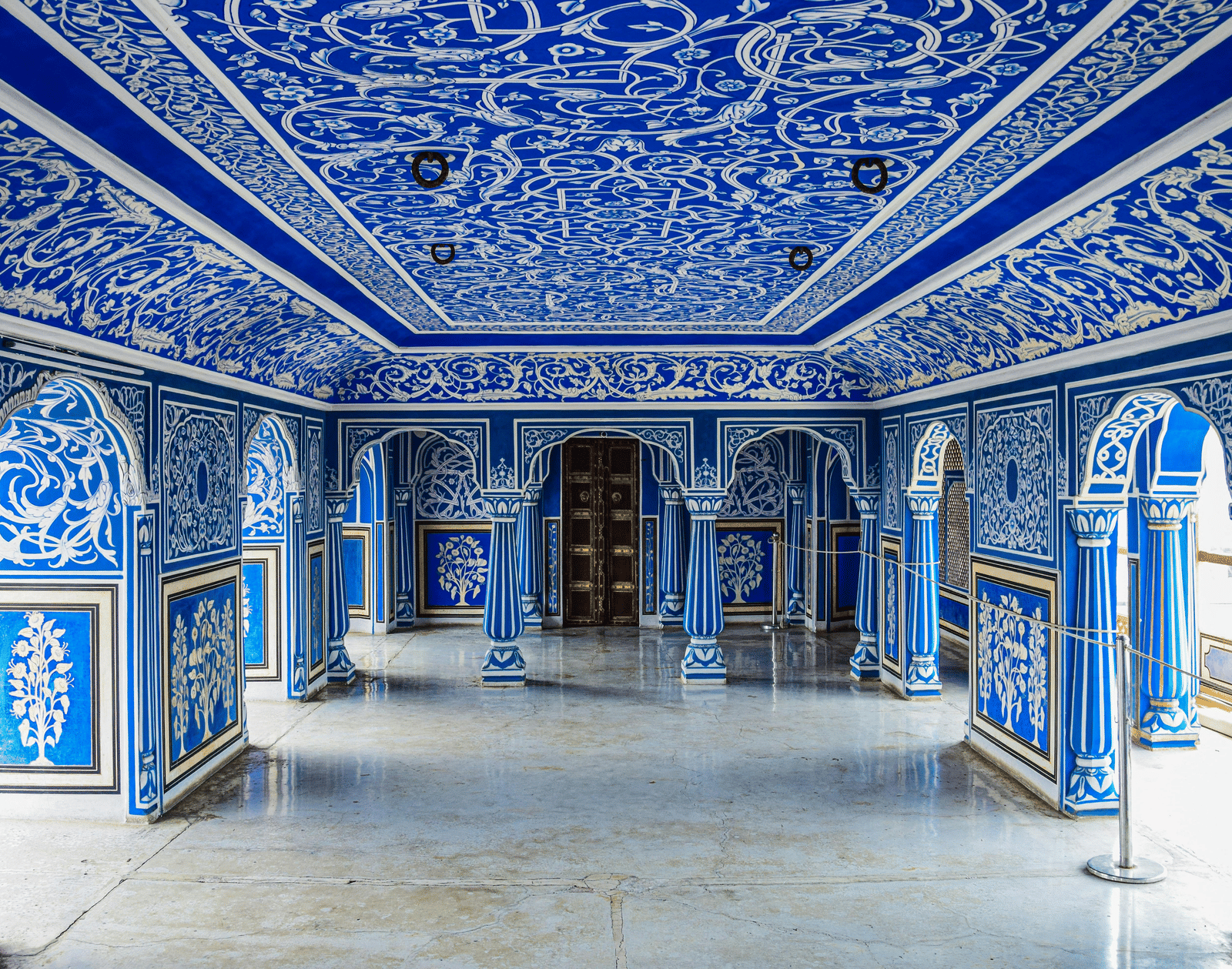 An ornately decorated blue hall with intricate artwork on the walls and ceiling, showcasing traditional Rajasthani architecture and design.