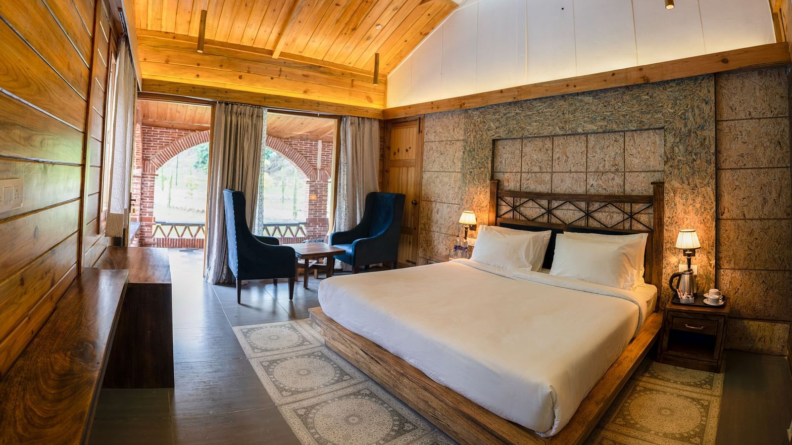 A large bed placed next to the chairs at Superior Room at the Sylvan Retreat, Dehradun.