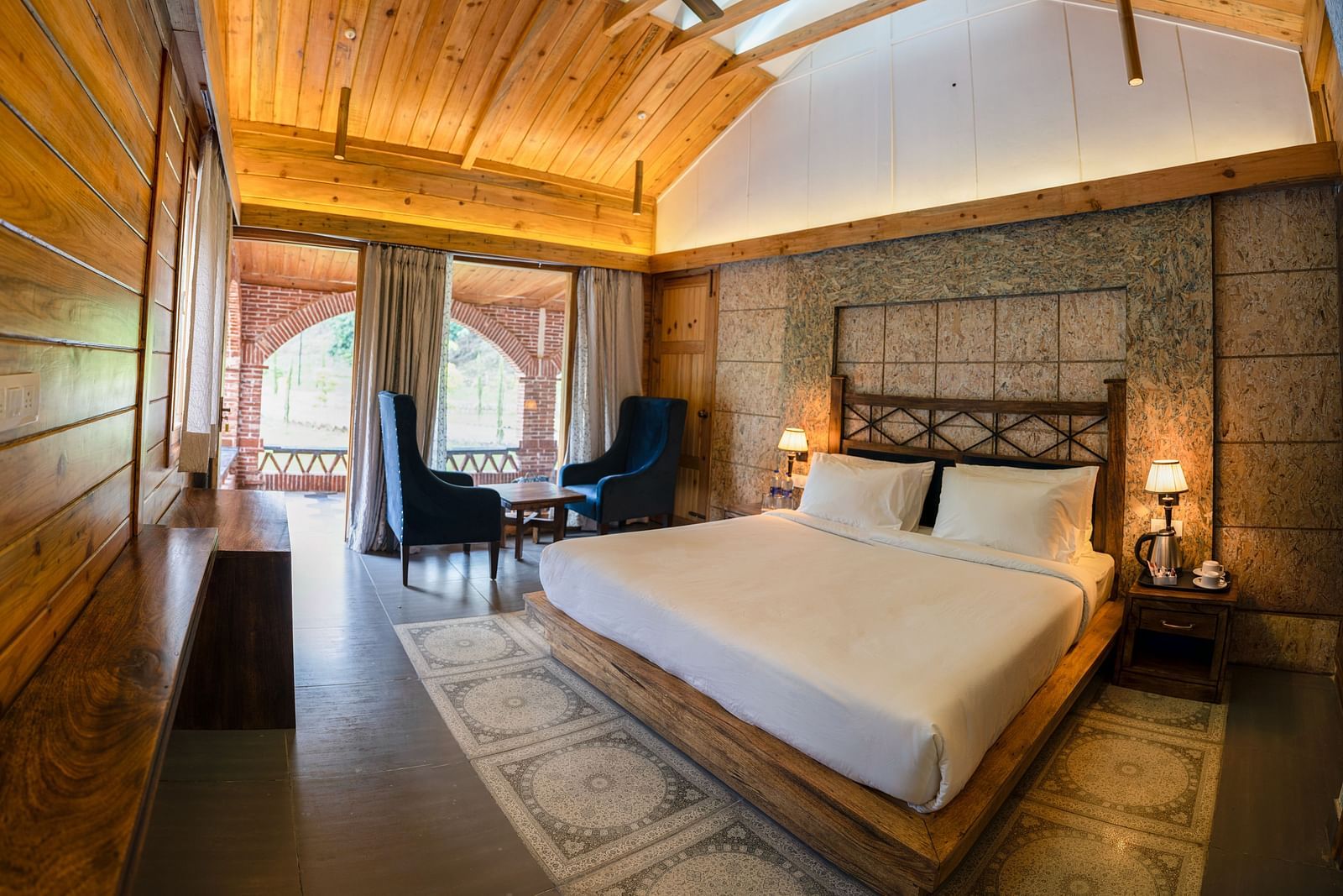 A large bed placed next to the chairs at Superior Room at the Sylvan Retreat, Dehradun.