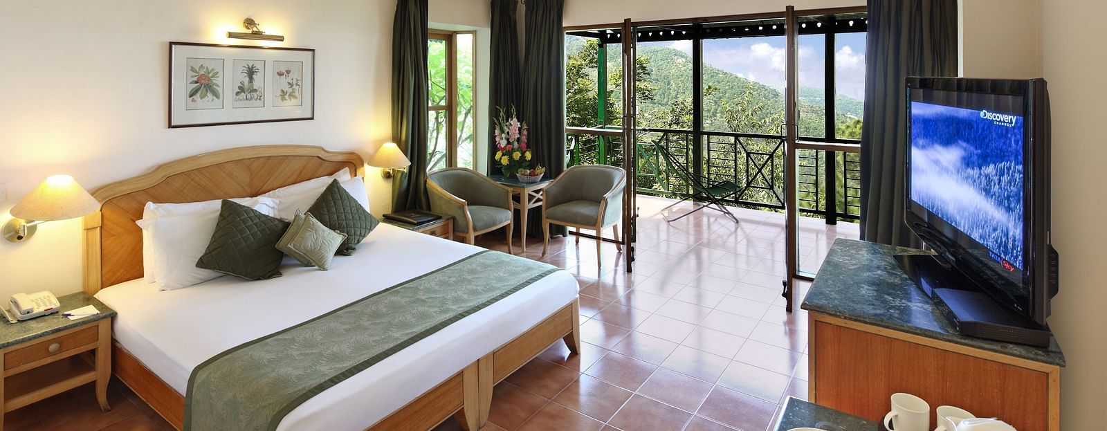 A bedroom with a sofa, a coffee table, a television, and a balcony offering a beautiful mountain view -  Baikunth resort, kasauli 