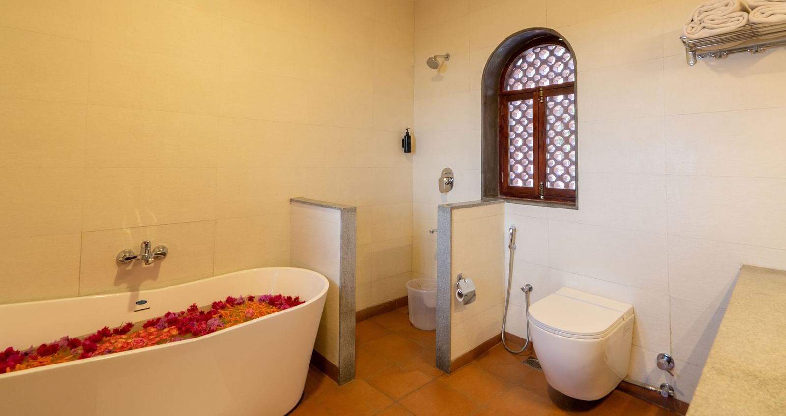 Luxurious bathroom with a rose petal-filled bathtub, elegant fixtures, and arched window. | Mango Hill, Yercaud