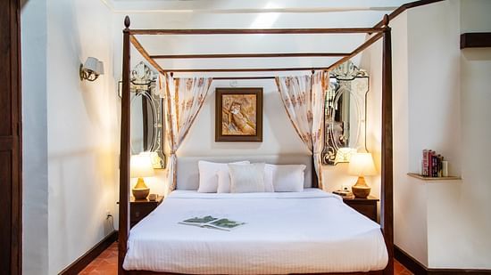 An image of a bedroom with poster beds and bedside table with lamp on either side at Lamrin Ucassaim Hotel, Goa