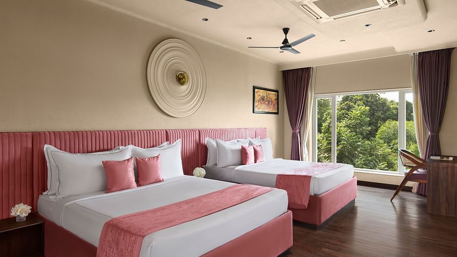 Super Deluxe Family Room with two large beds featuring pink and white bedding, and a window overlooking lush green trees at DGV Resort by Treat, Silvassa