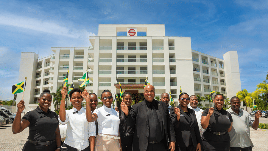 A group of people outside S hotels building holding the flags of Jamaica.