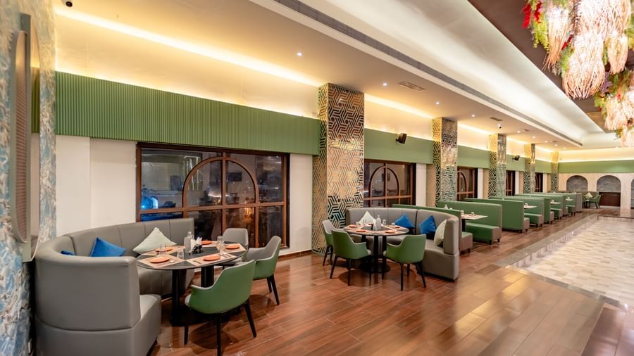 The restaurant space with orange and green seating and intricate ceiling decorations | Pravasa Hotel, Vijayapura