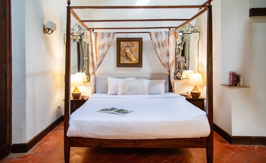 An image of a bedroom with poster beds and bedside table with lamp on either side at Lamrin Ucassaim Hotel, Goa