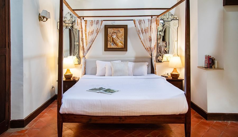An image of a bedroom with poster beds and bedside table with lamp on either side at Lamrin Ucassaim Hotel, Goa