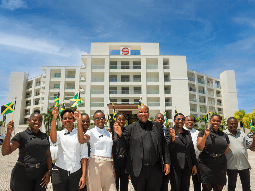 A group of people outside S hotels building holding the flags of Jamaica.