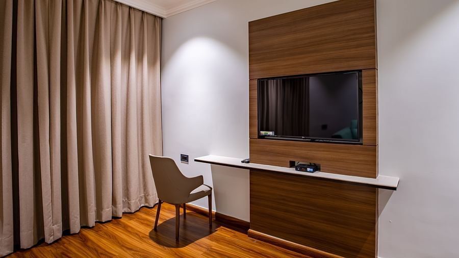 a tv wall mounted with a study table on the side - Wedlock Greens Hotel Resorts Dhanbad