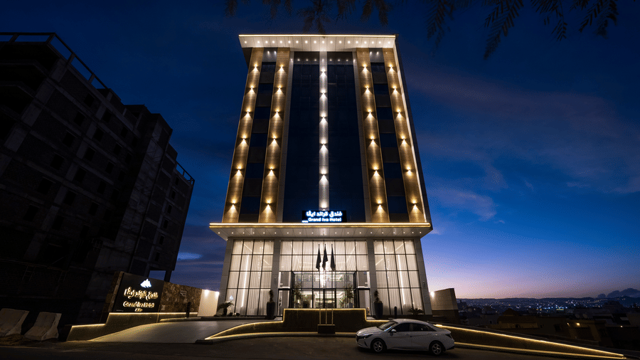 Exterior of the multi-storey Grand Iva Hotel, Abha, seen with a vibrantly coloured sky in the background, and the building being brightly lit.