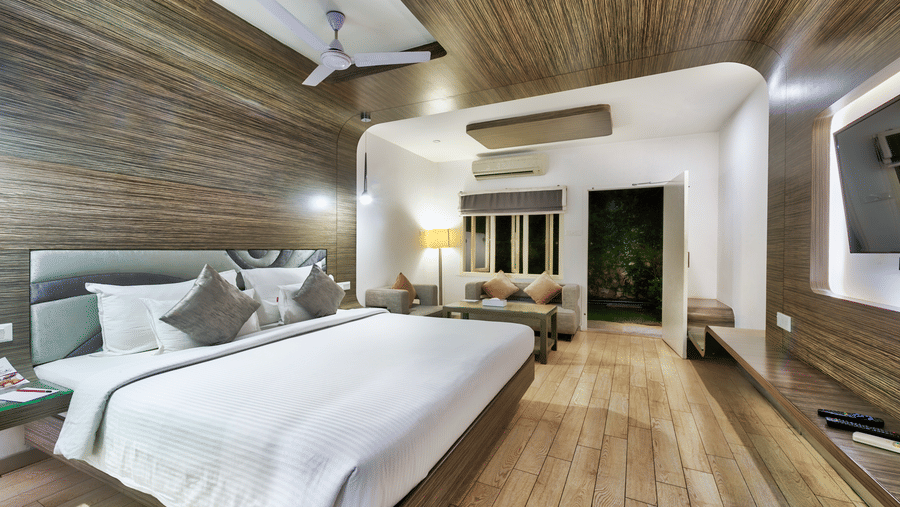 A spacious room with a king size bed, wooden flooring, seating area and ceiling fan at Grande Bay Resort & Spa, Mamallapuram.