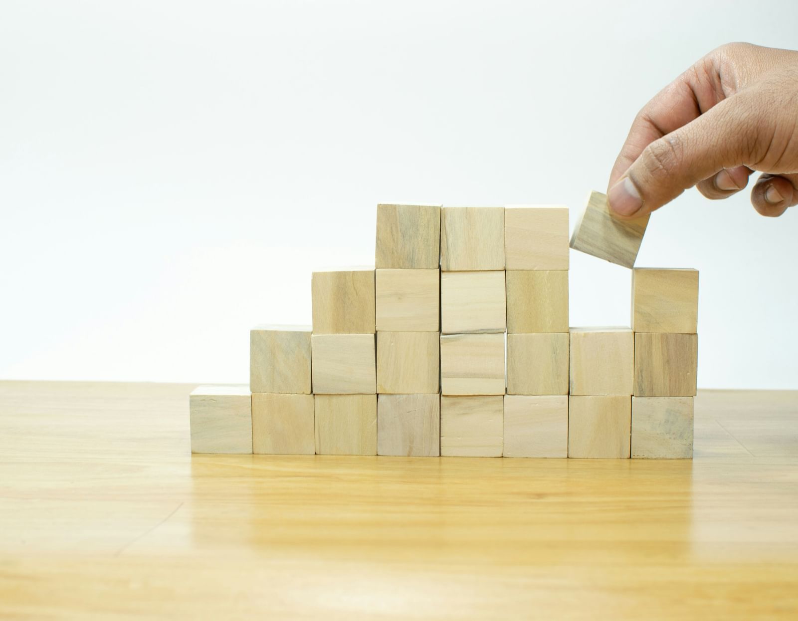 A person stacking up wooden blocks over a wooden surface.