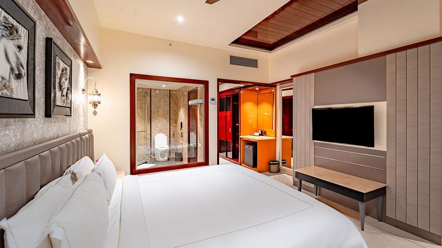 Deluxe Room at Crescent Spa & Resort, Indore, features a spacious bed with a wall-mounted television directly opposite, and two photo frames above the headboard