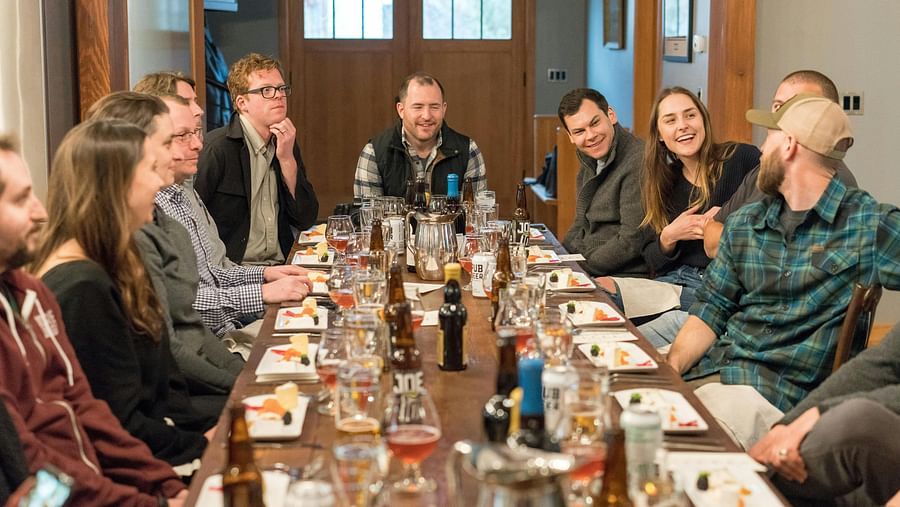 Group of people enjoying a meal and conversation around a long dining table set with food, drinks, and glassware in a  indoor setting.