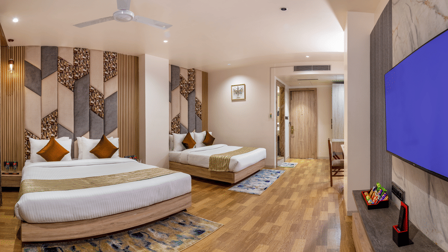 Spacious room at Lords Inn Sangam, Bhopal with twin beds, patterned wall panels, wooden flooring, and a wall-mounted television.