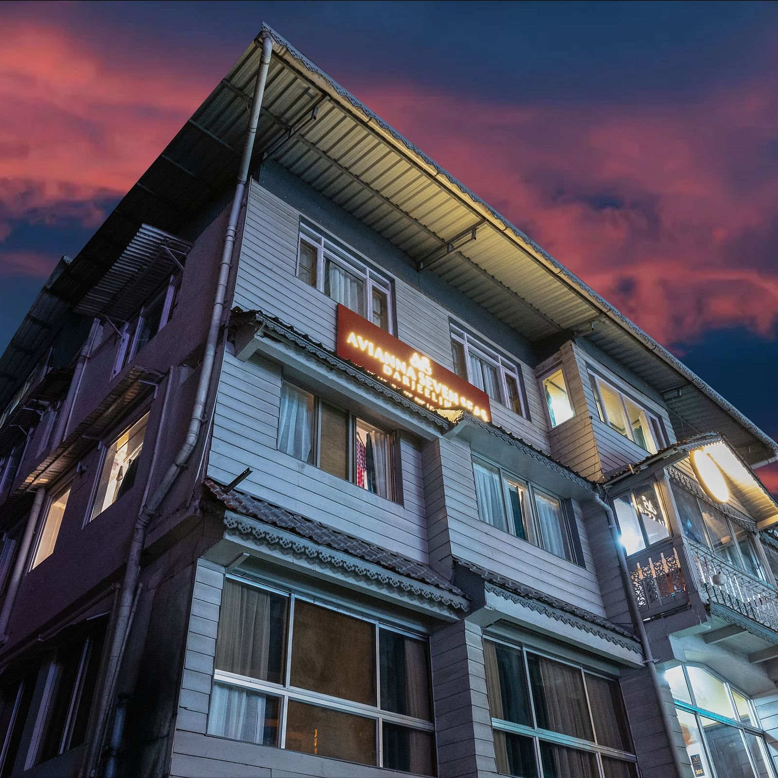 Facade view of Avianna Seven Seas, Darjeeling at dusk with dramatic pink and blue sky, warmly lit windows, and signage glowing on the upper facade.