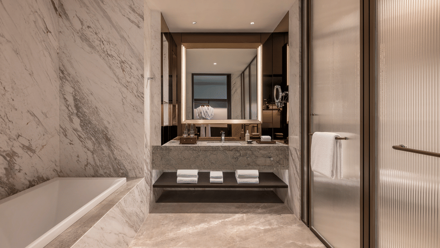Bright marble bathroom at The Residency Signature Madurai equipped with a bathtub, a single sink vanity, a mirror, and a glass shower door.