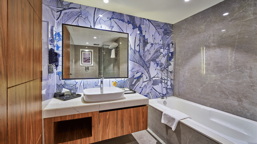 A bathroom featuring a white bathtub, a wooden vanity unit with a countertop basin, and a mirror | HHI Varanasi