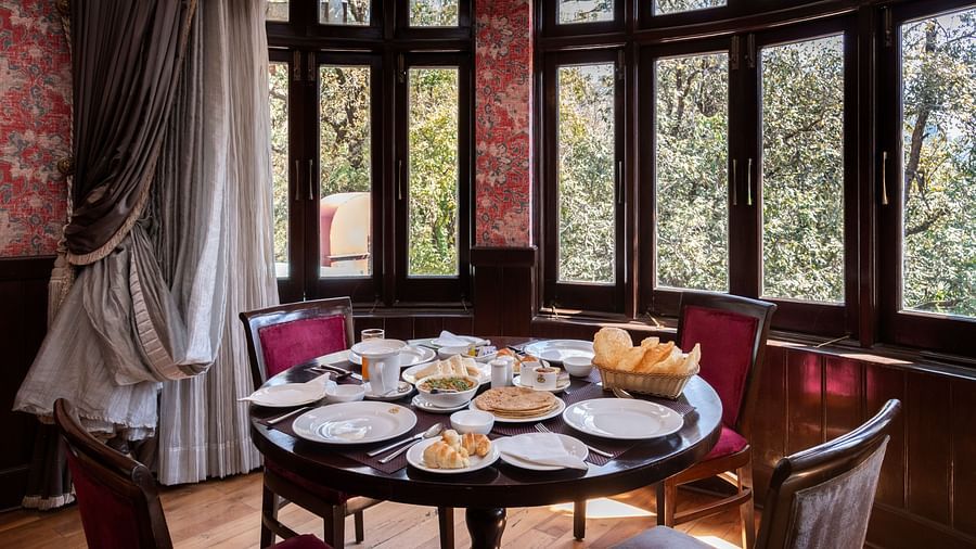 A dining space with chairs, large windows overlooking a forest and a table adorned with various snacks - The Claridges Nabha Residence, Mussoorie