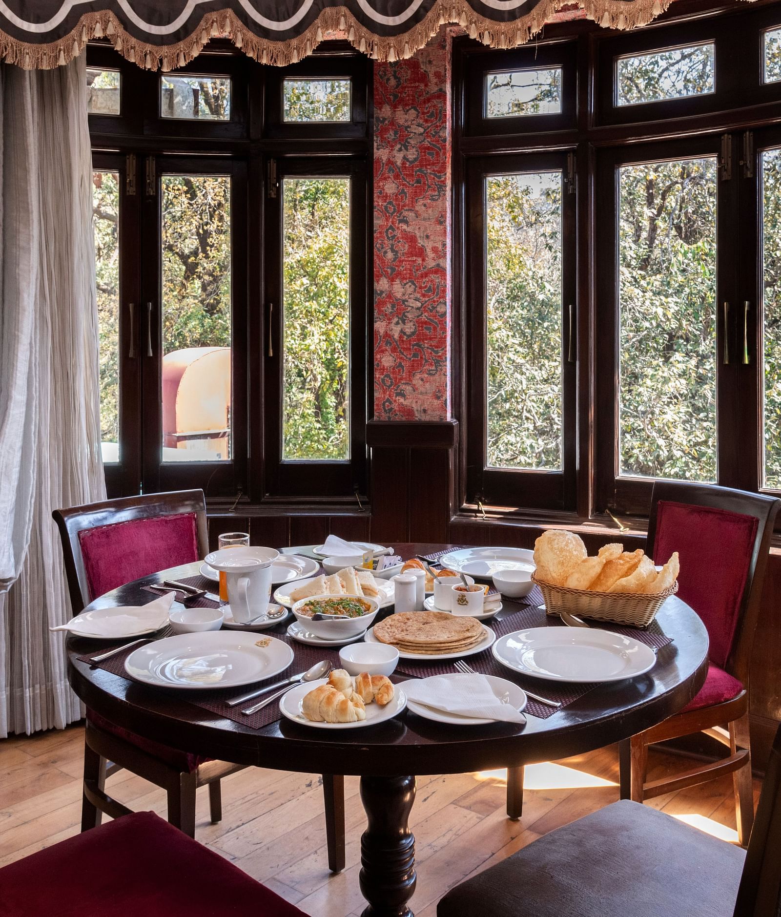 A dining space with chairs, large windows overlooking a forest and a table adorned with various snacks - The Claridges Nabha Residence, Mussoorie