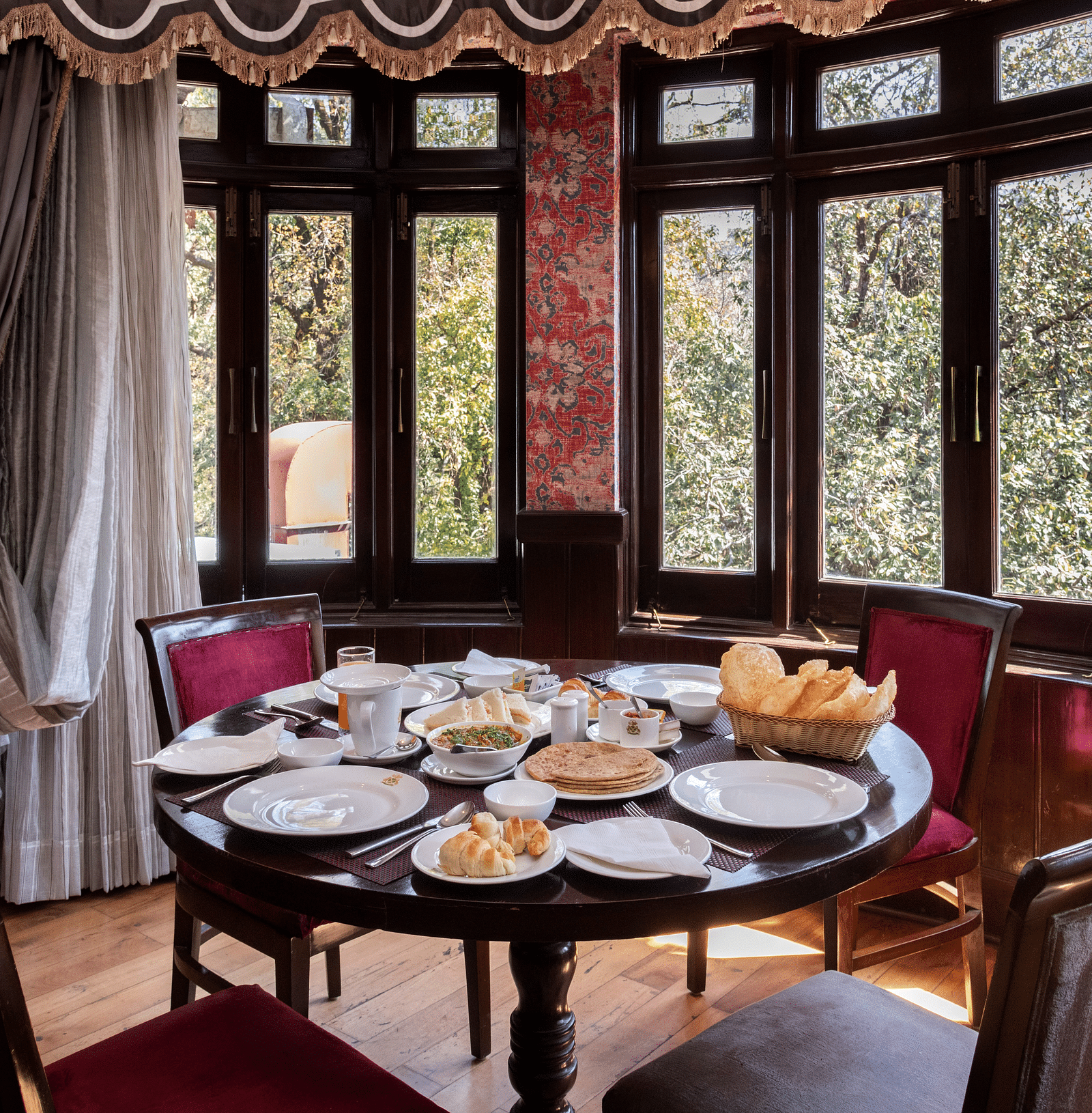 A dining space with chairs, large windows overlooking a forest and a table adorned with various snacks - The Claridges Nabha Residence, Mussoorie