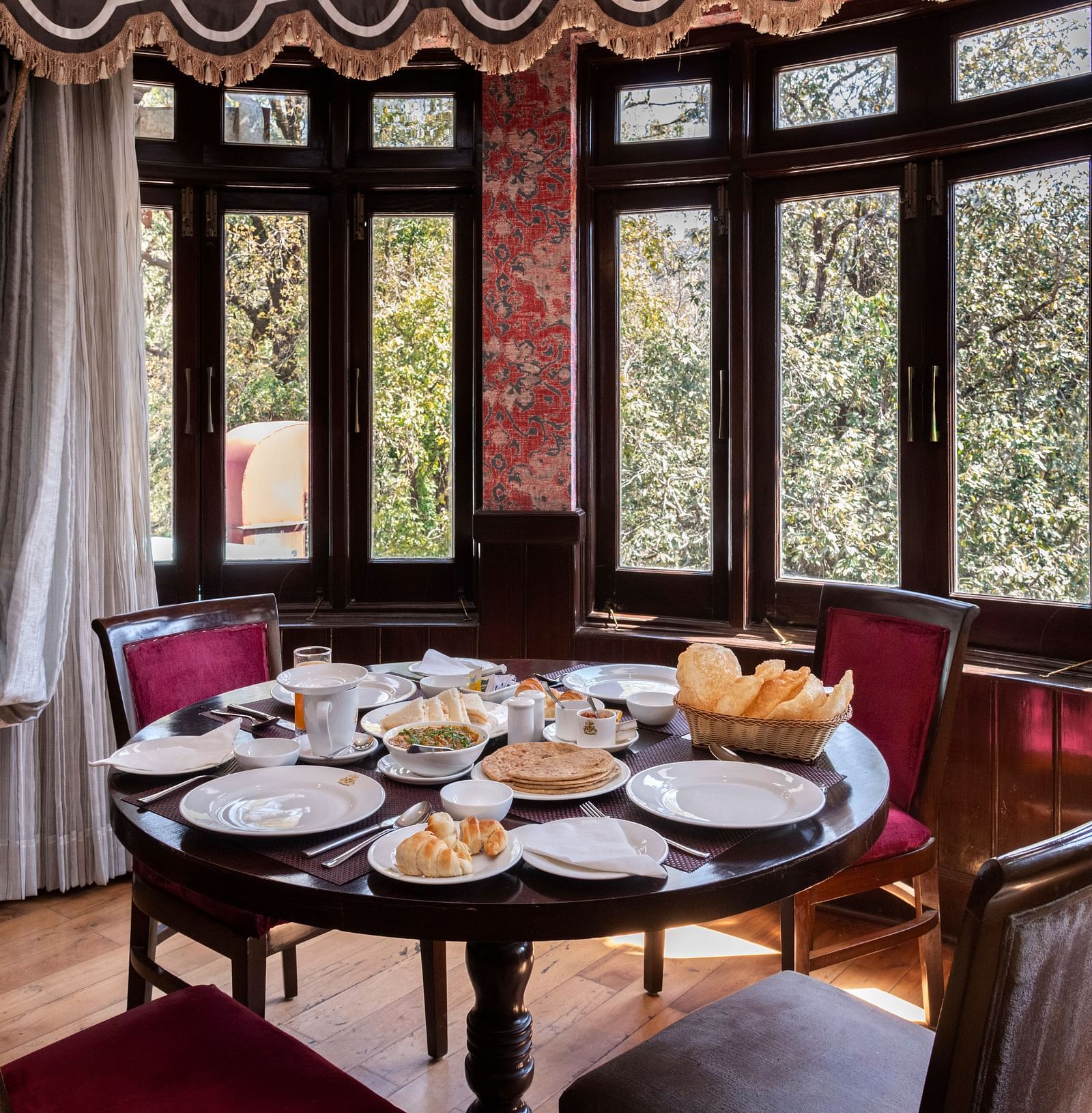 A dining space with chairs, large windows overlooking a forest and a table adorned with various snacks - The Claridges Nabha Residence, Mussoorie
