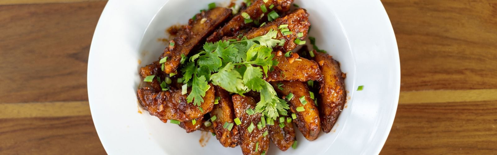 image of a white plate with potato wedges topped with fresh coriander leaves
