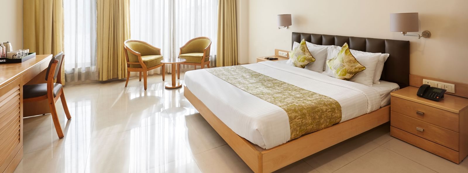 A well-lit hotel room at Monday Hotels Mahape, Navi Mumbai, with a large bed, seating area, and wooden furniture.