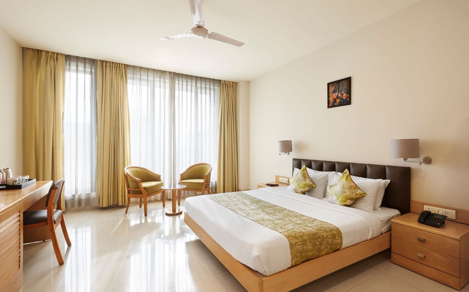 A well-lit hotel room at Monday Hotels Mahape, Navi Mumbai, with a large bed, seating area, and wooden furniture.