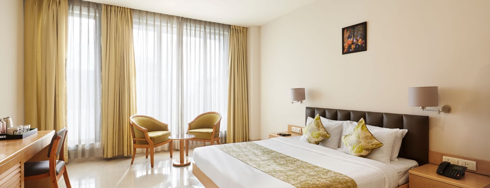 A well-lit hotel room at Monday Hotels Mahape, Navi Mumbai, with a large bed, seating area, and wooden furniture.