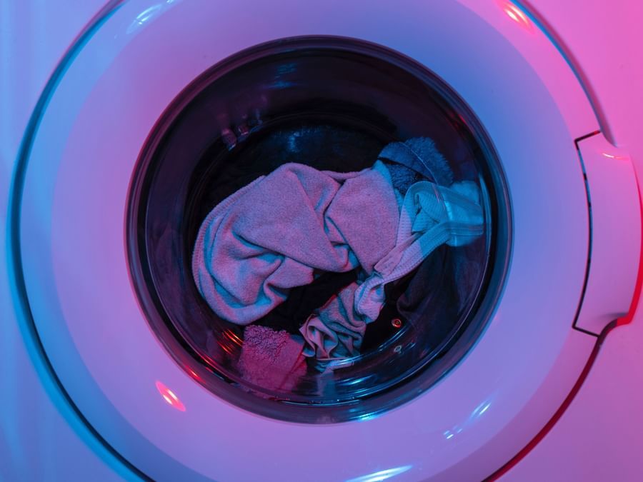 A zoom shot of a front load washing machine with clothes in it and saturated purple light being reflected on the washing machine's door