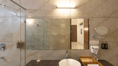 A contemporary bathroom with a large mirror over a dark counter, a white basin, and glass shower enclosure, showing toiletries - Pride Premier Solitaire Dehradun